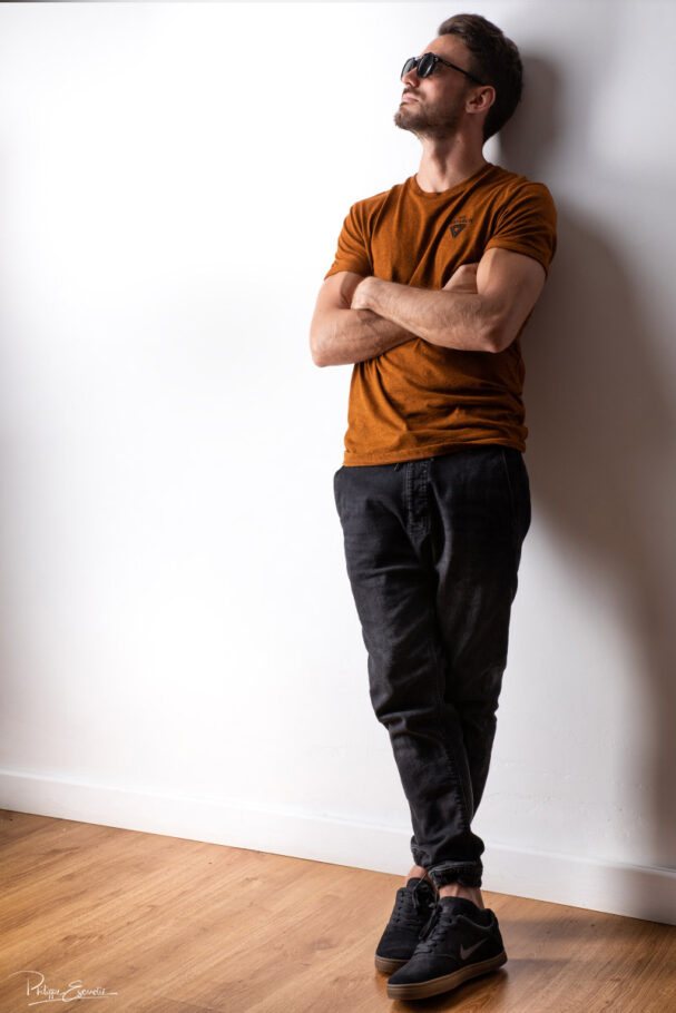 portrait mannequin d''un jeune debout contre un fond blanc les bras croisés portant des lunettes de soleil