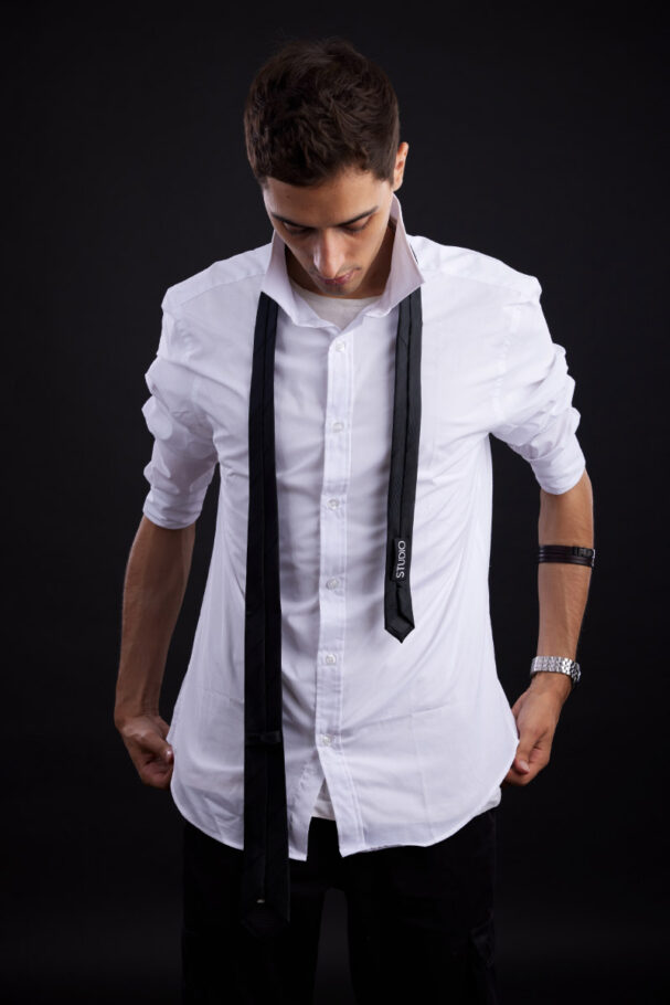 Jeune homme en studio sur fond sombre portant une chemise blanche et une cravate détachée