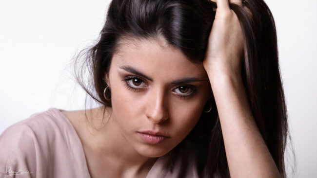 Une femme aux longs cheveux portant une chemise marron une main dans les cheveux