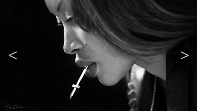 photo en noir et blanc du visage d'une femme qui tient dans sa bouche une croix