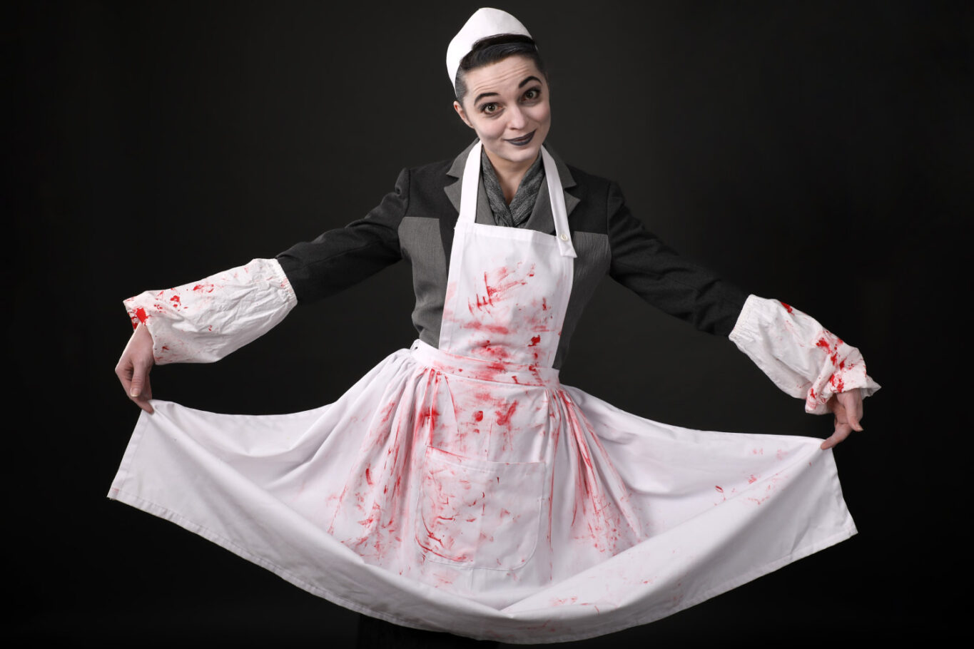 Une femme en uniforme d'infirmière, avec des taches de sang sur son tablier fait une révérence avec son tablier