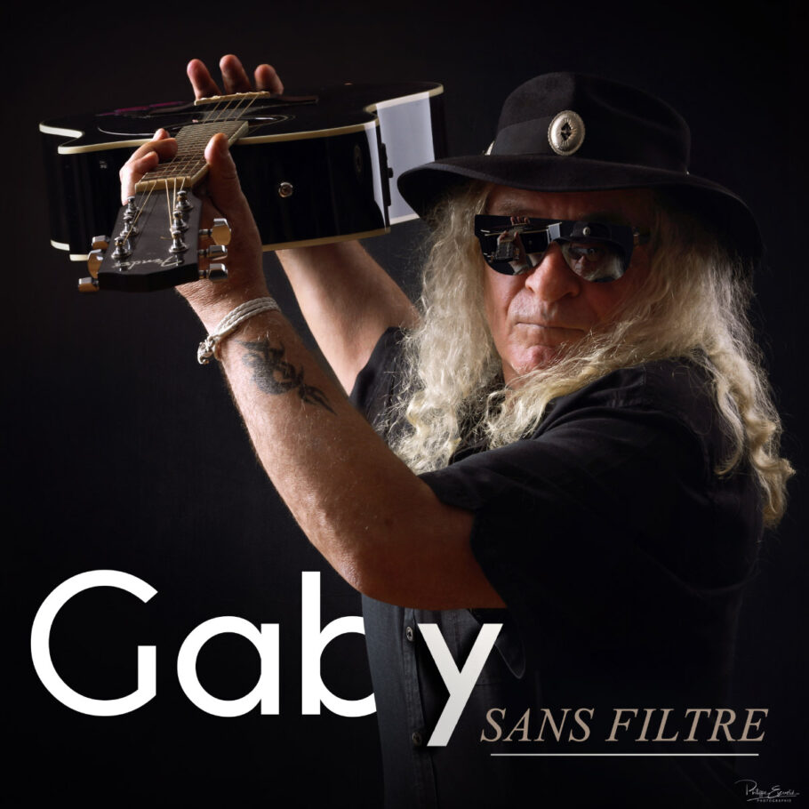 Portrait d'un musicien, Gaby, tenant une guitare à bout de bras avec des lunettes noires et un chapeau