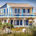 chalet en bois blanc et bleu sur pilotis avec de la végétation autour