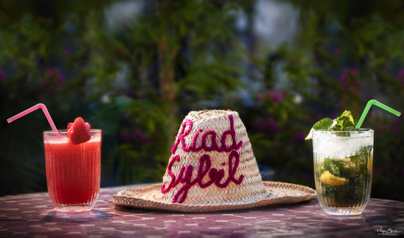 Un chapeau en paille avec dessus l'inscription Riad sybil et deux cocktails avec pailles autour du chapeau