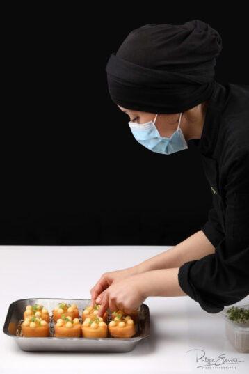 Une femme masquée s'affaire à la préparation de médaillons de pomme de terre