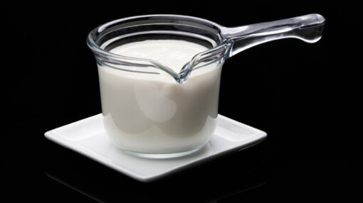 Une casserole en verre contenant du lait, posée sur une assiette blanche avec un fond noir en arrière plan
