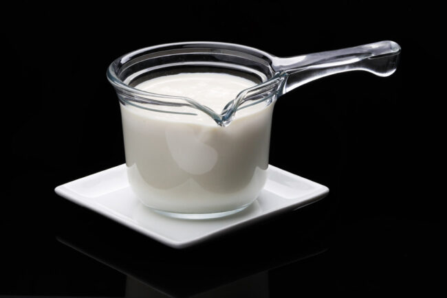 Une casserole en verre contenant du lait, posée sur une assiette blanche avec un fond noir en arrière plan