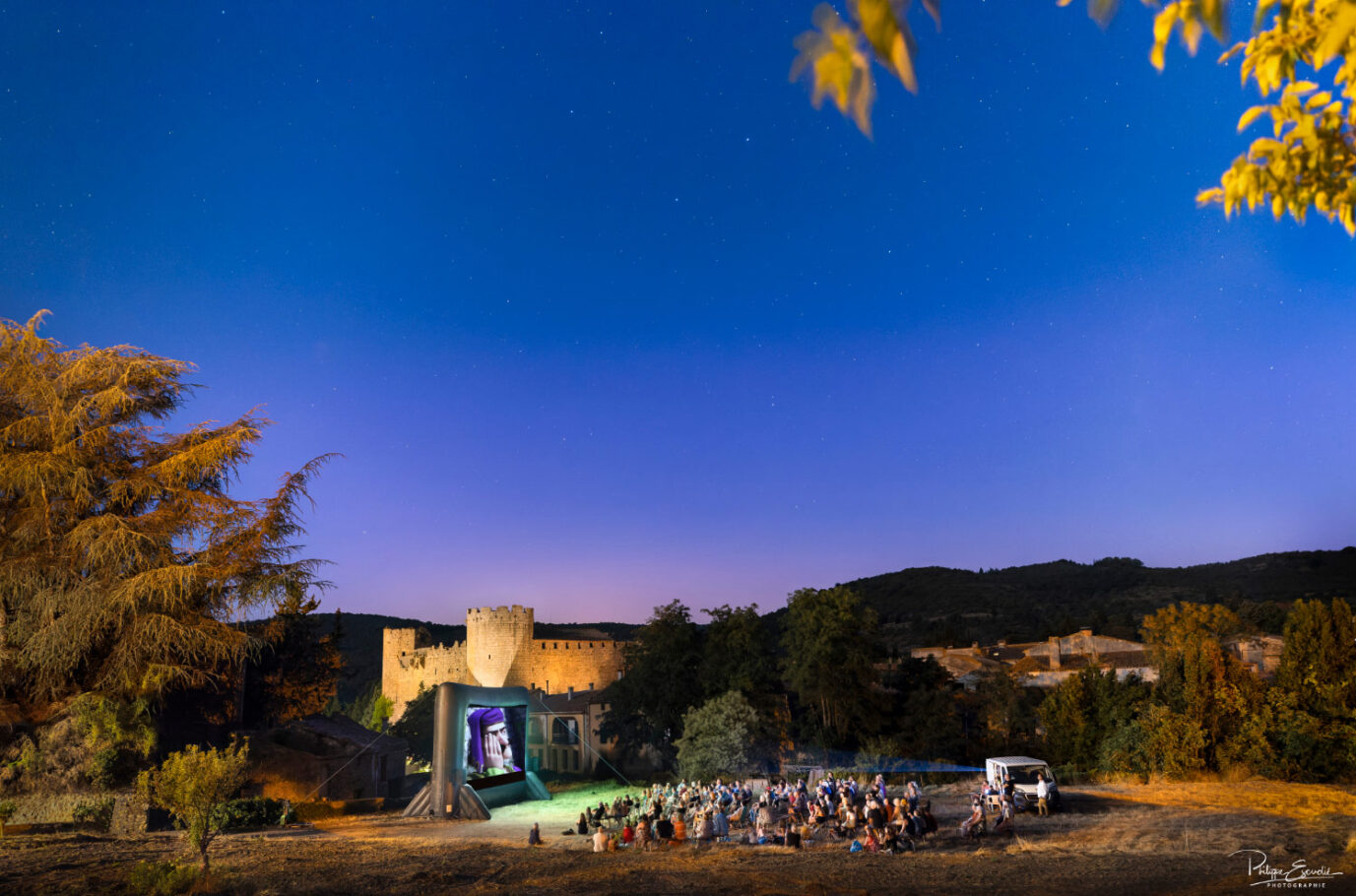 projection audiovisuelle nocturne en pleine campagne avec le public assis et un château en ruine en arrière plan
