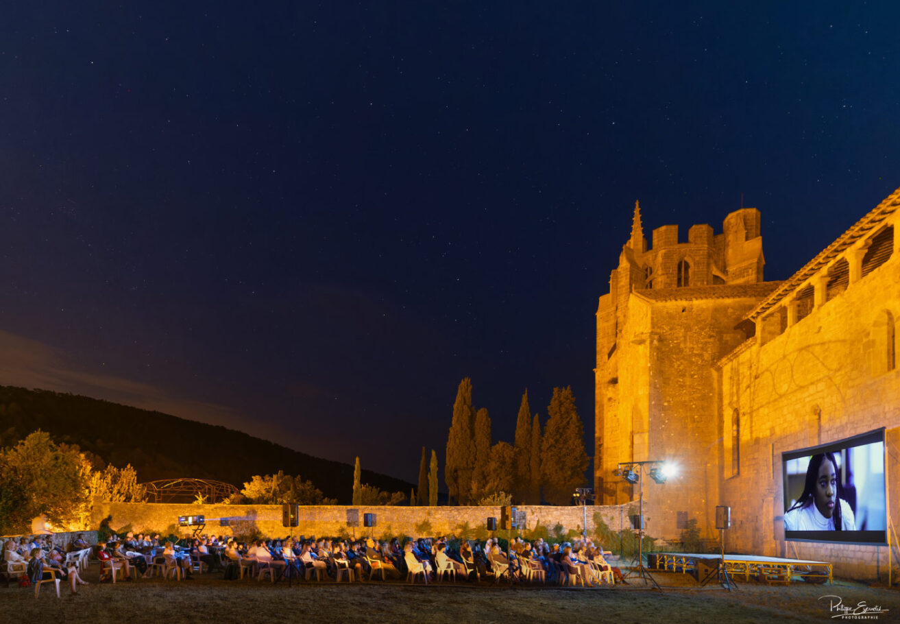 Public assis assistant à une projection audiovisuelle nocturne devant l'abbaye de Lagrasse