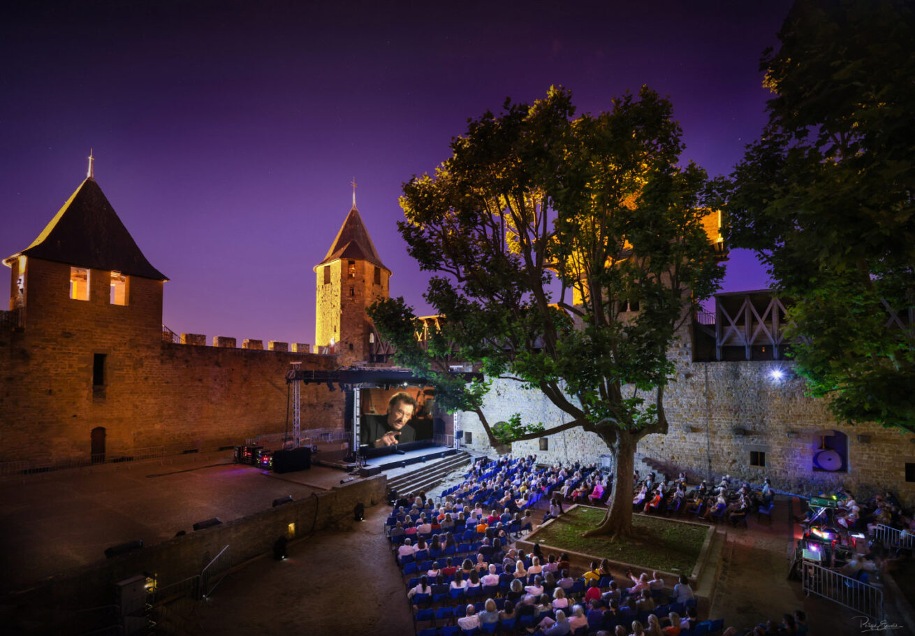 Projection nocturne dans la cité de Carcassonne d'un documentaire sur Johnny Hallyday avec un public nombreux assis sur des chaises