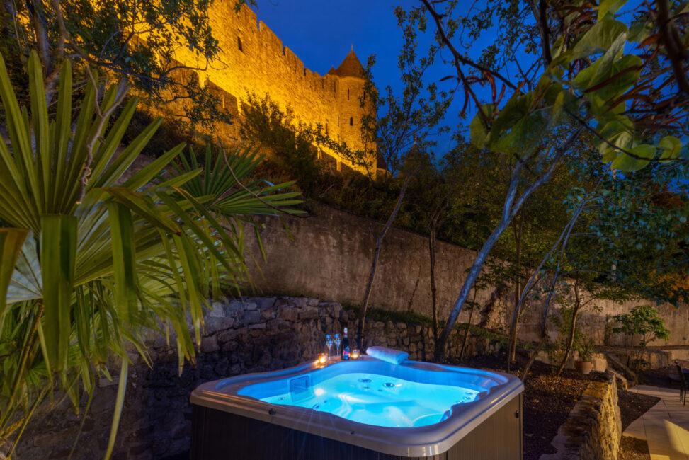 jacuzzi éclairé de nuit dans un jardin avec en arrière plan les murailles de la Cité de Carcassonne
