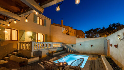Maison avec piscine et patio illuminés la nuit avec au premier plan un apéritif dressé sur une petite table ronde