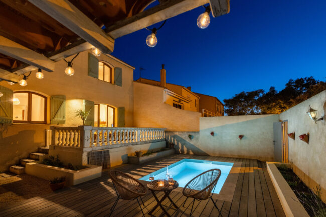 Maison avec piscine et patio illuminés la nuit avec au premier plan un apéritif dressé sur une petite table ronde