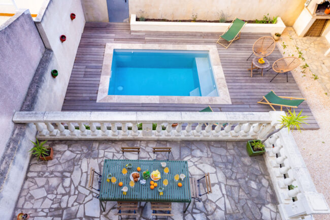 Focus sur Rémi Alba, Conciergerie "OC Keys" 14 vue en hauteur d'une piscine et d'une terrasse sur laquelle il y a une table en fer vert avec un petit déjeuner dressé