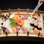 Une personne utilise des baguettes pour saisir des sushis sur un plateau, mettant en avant la culture culinaire japonaise.