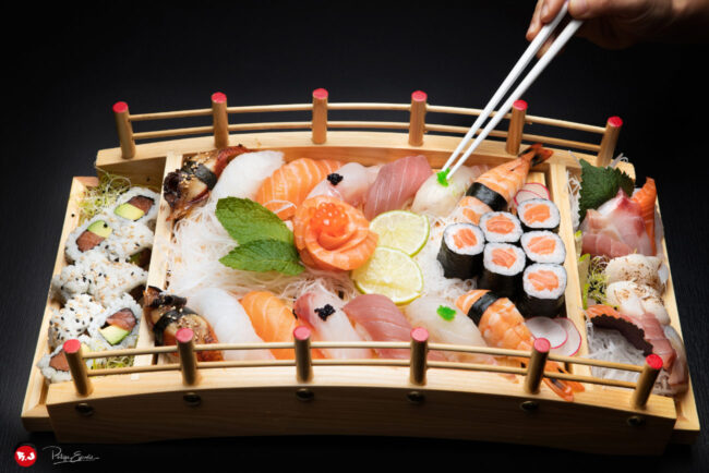 Une personne utilise des baguettes pour saisir des sushis sur un plateau, mettant en avant la culture culinaire japonaise.
