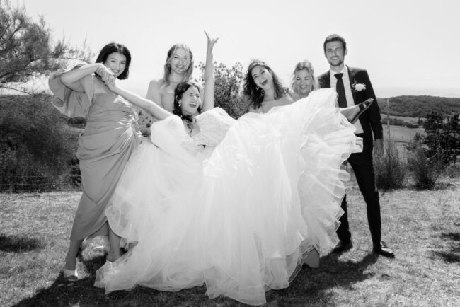 Photo en noir et blanc d'un groupe de mariage, ambiance festive avec la mariée tenue en l'air par ses témoins