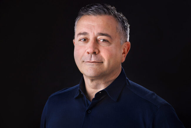 portrait d'un homme souriant aux tempes grises sur fond sombre