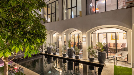 une piscine et un espace patio de nuit avec en arrière plan une façade vitrée éclairée créant une atmosphère de tranquillité