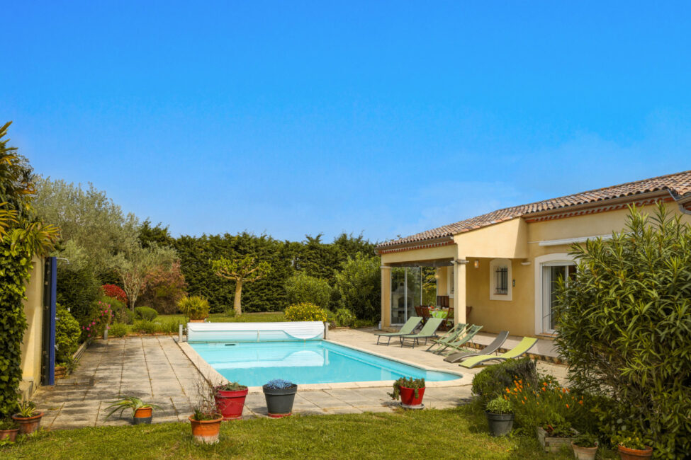 une jardin verdoyant avec une piscine, des bains de soleil et la façade d'une maison