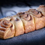 Brioche avec un motif en spirale, délicatement dorée et appétissante, posée sur un fond sombre saupoudré de sucre glace