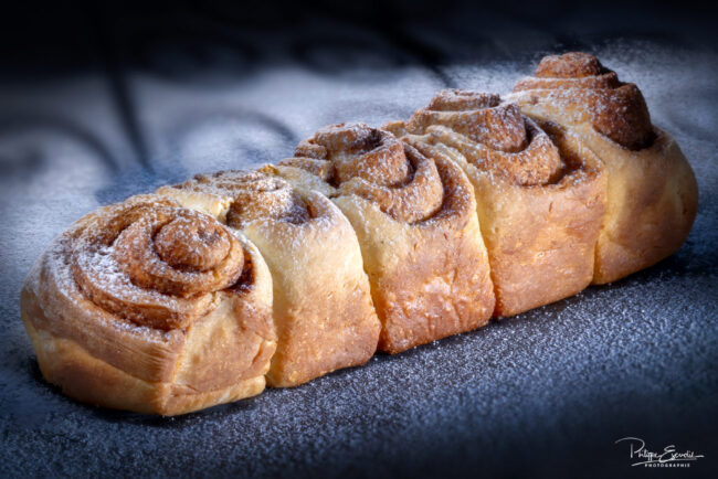 Brioche avec un motif en spirale, délicatement dorée et appétissante, posée sur un fond sombre saupoudré de sucre glace