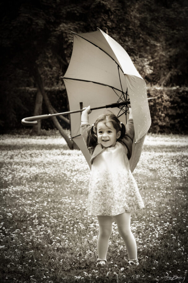 photo noir et blanc dans une nature fleurie d'une petite fille qui tient dans les mains un parapluie