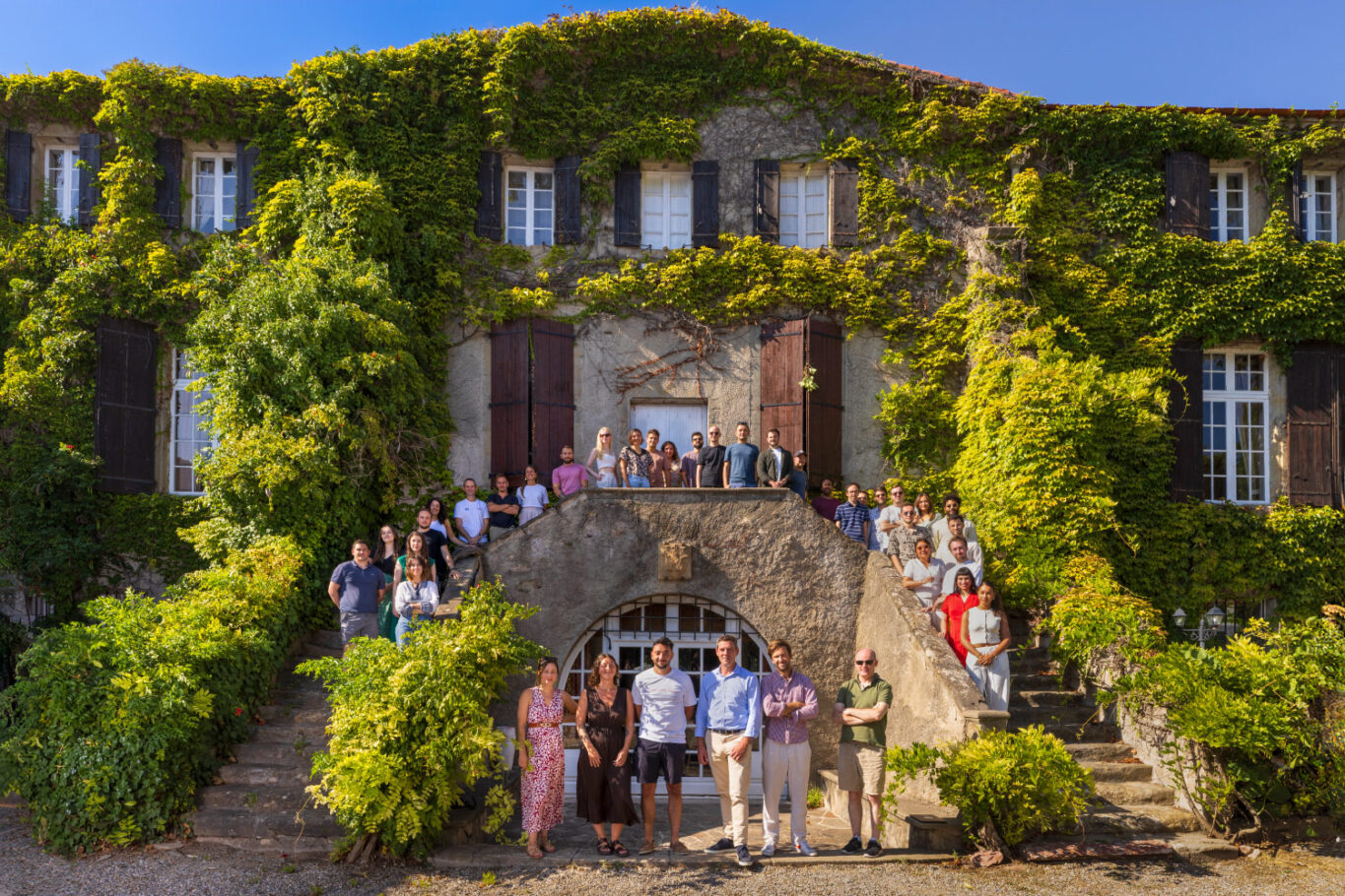 Photo de groupe devant une vieille et belle bâtisse avec une façade verdoyante de végétation