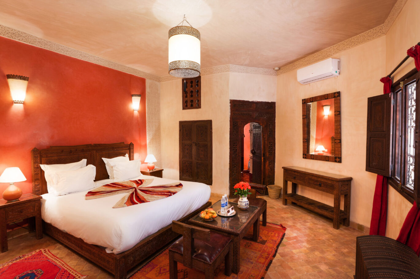 Une grande chambre de riad aux tons crème et orange avec un grand lit aux draps blancs et de nombreux luminaires