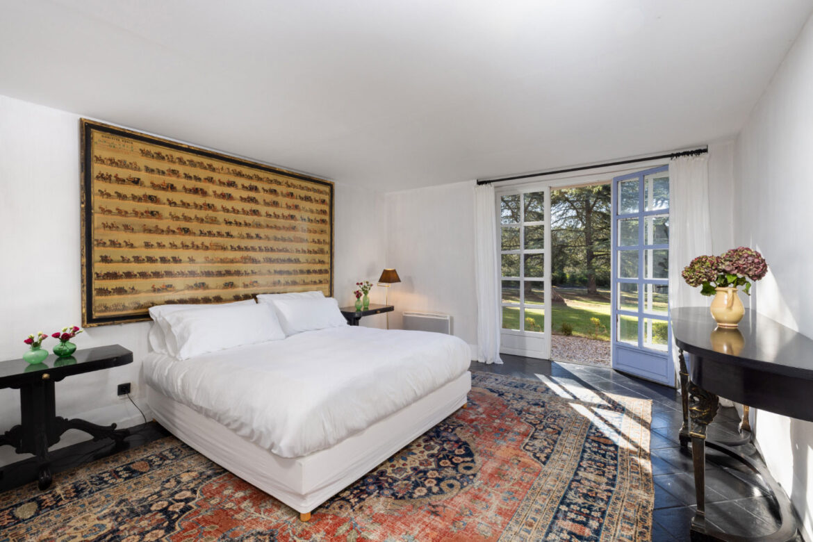 Chambre lumineuse avec lit double, grande baie vitrée ouvrant sur un jardin et décoration élégante