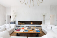Salon élégant avec grande cheminée moderne, canapé blanc, table en bois et statue en marbre, dans une décoration épurée et raffinée