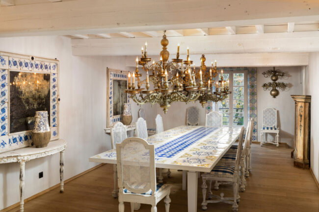 Salle à manger élégante avec grande table en céramique bleue et blanche, chaises en bois sculpté et lustre doré imposant
