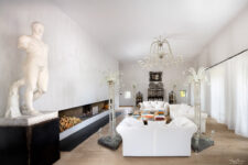 Salon luxueux avec décoration classique et design, grande cheminée moderne, canapé blanc et statue en marbre, éclairé par un lustre en cristal et des luminaires en verre