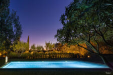 Piscine éclairée au crépuscule, entourée d’arbres et de végétation luxuriante, avec une statue en arrière-plan