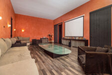 Salle de cinéma privée avec grand canapé, table en verre, écran de projection et mur terracotta