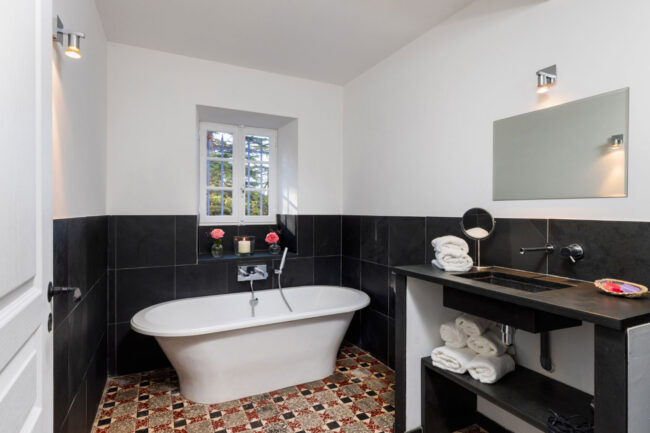 Salle de bain élégante avec baignoire îlot, sol en carreaux vintage, murs noirs et blancs, et lumière naturelle - photographie immobilière
