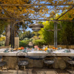 Table en pierre dressée pour le petit-déjeuner sous une pergola ombragée, avec vue sur un jardin luxuriant