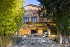 Table en pierre dressée pour le petit-déjeuner sous une pergola ombragée, avec vue sur un jardin luxuriant