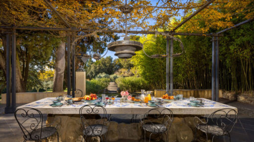 Table en pierre dressée pour le petit-déjeuner sous une pergola ombragée, avec vue sur un jardin luxuriant