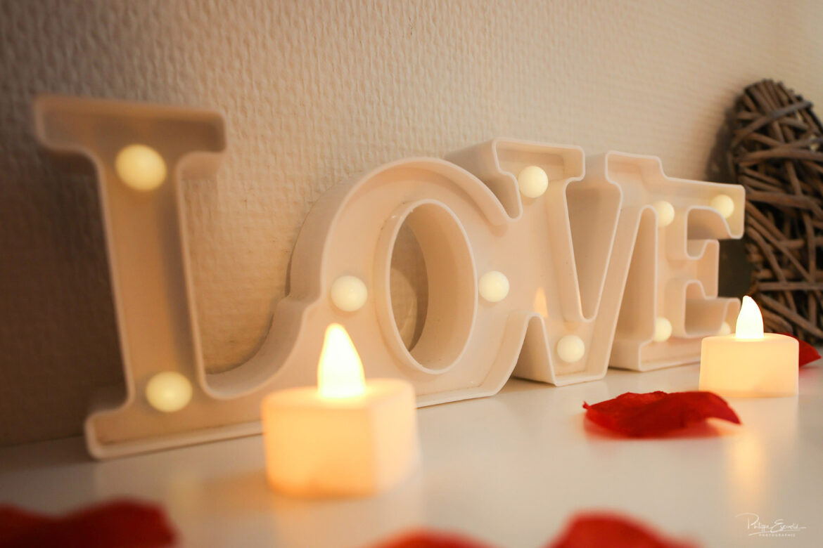 Décoration romantique avec lettres LOVE lumineuses, bougies et pétales rouges