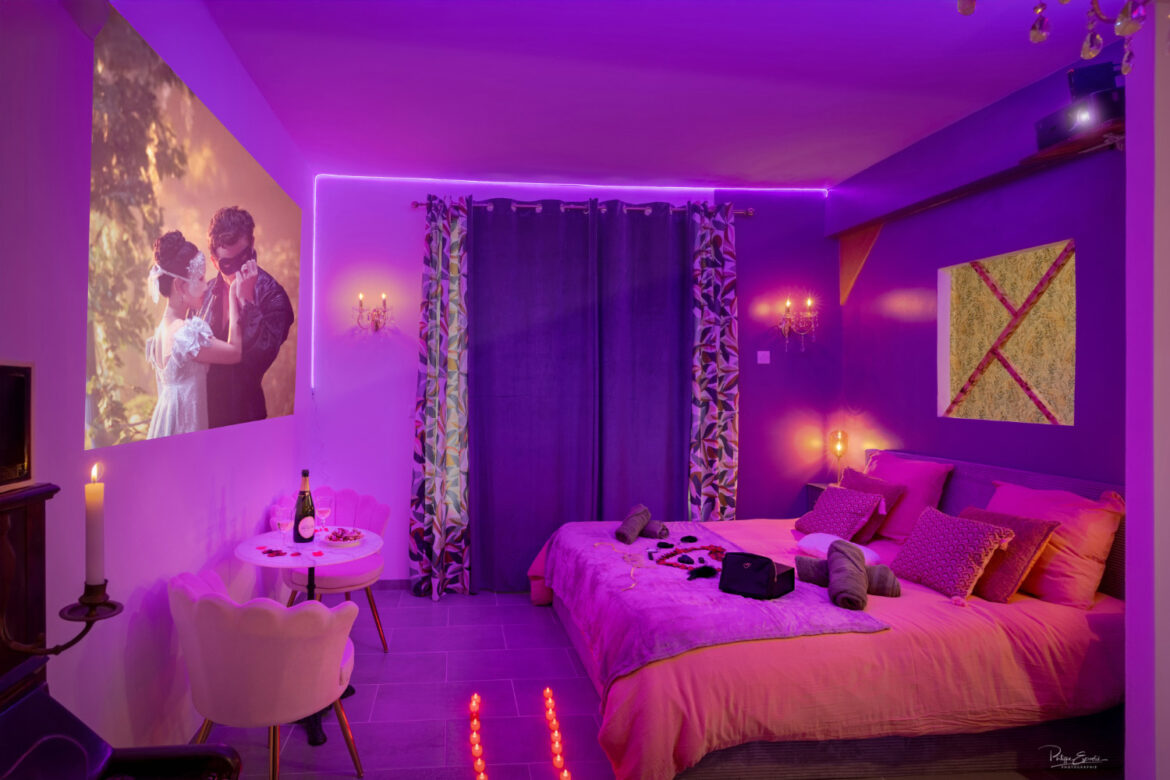 Chambre romantique avec éclairage tamisé violet, projection de film, lit double et accessoires dans une love room
