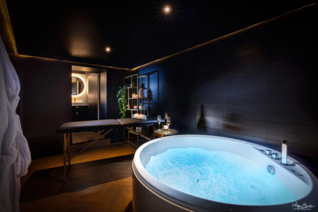 Espace bien-être avec jacuzzi, table de massage et ambiance tamisée dans une love room à Carcassonne