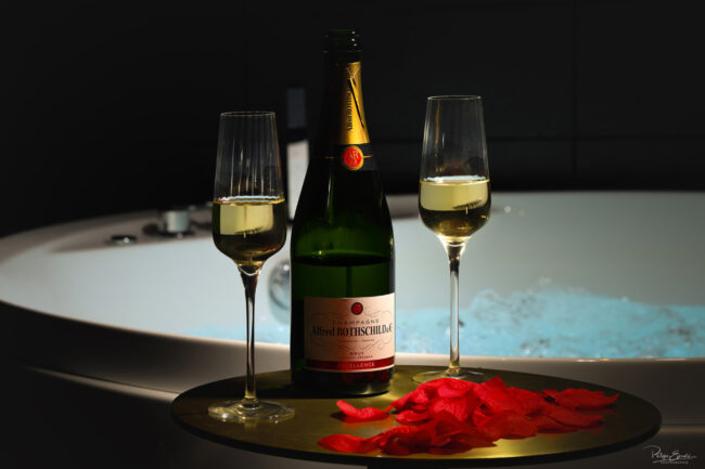 Coupe de champagne et pétales de rose près d’un jacuzzi dans une love room à Carcassonne – photographie immobilière romantique