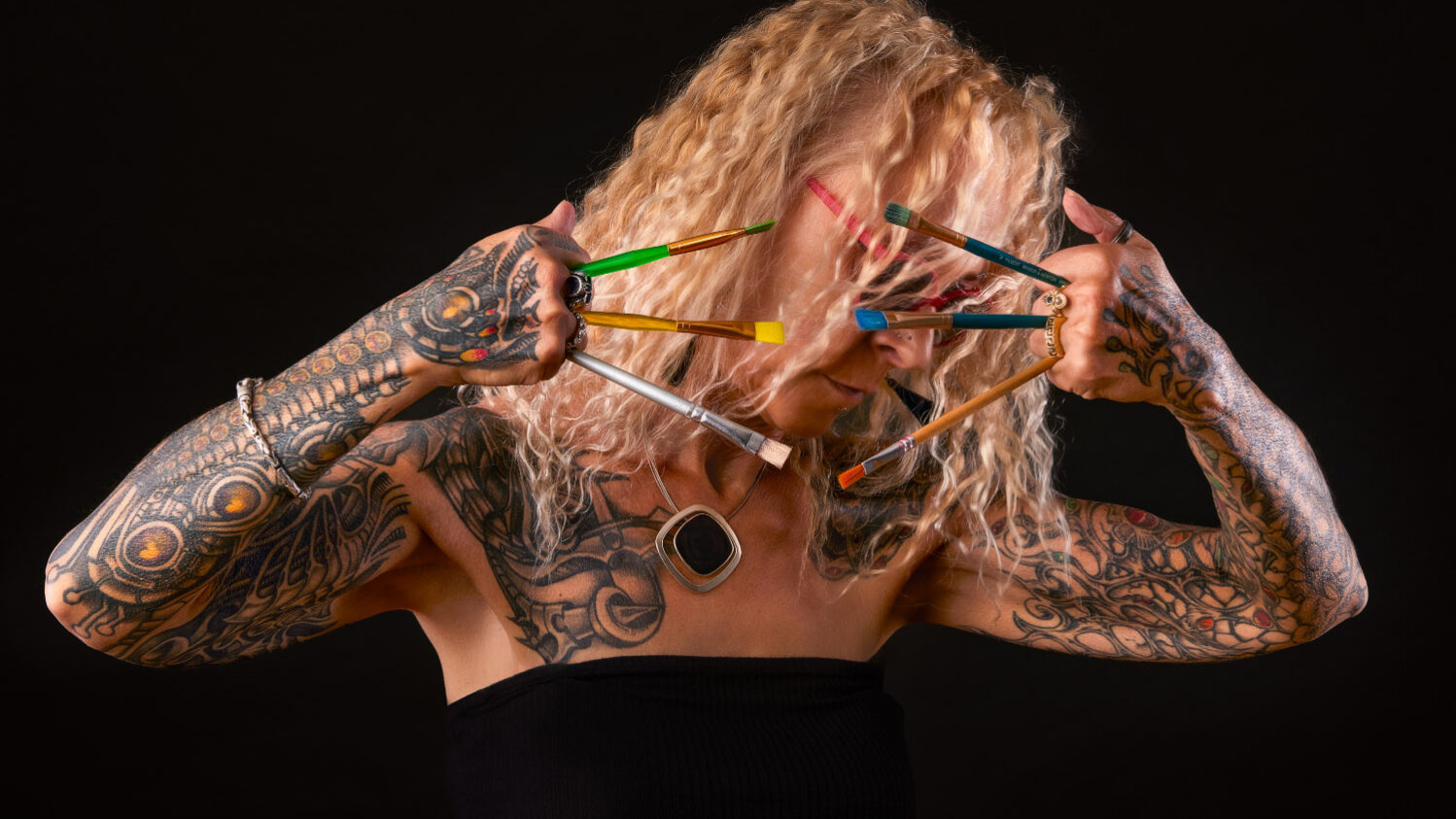 Photo artistique en studio d’une femme tatouée avec des pinceaux devant le visage – portrait par photographe à Carcassonne