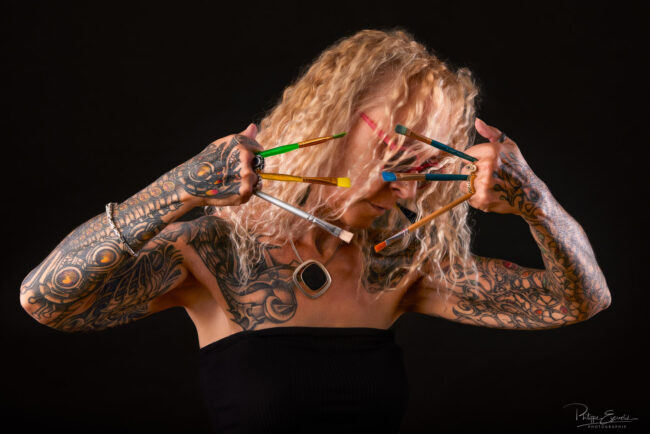 Photo artistique en studio d’une femme tatouée avec des pinceaux devant le visage – portrait par photographe à Carcassonne