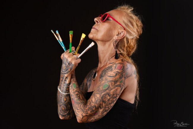 Photographe Portrait : Focus sur Cristelle Bernardinello, artiste peintre 3 Portrait studio d’une femme tatouée de profil avec pinceaux à la main et des lunettes rouge – photo pour book
