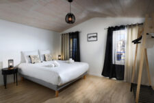 Chambre lumineuse sous combles avec lit double, rideaux bicolores, deux tables de chevet et plafond en bois clair