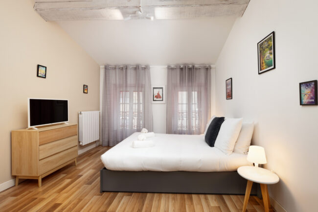 Chambre contemporaine avec lit double, télévision à écran plat, sol en bois et poutres apparentes