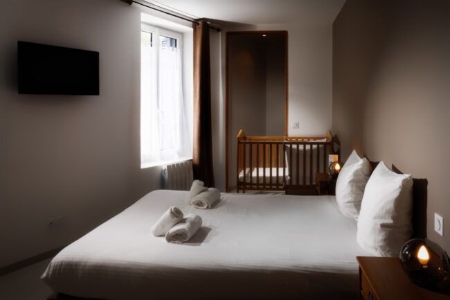 Petite chambre avec lit double, lumière douce, lit bébé en bois et rideaux chocolat