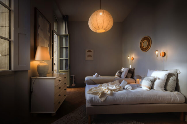 Chambre design avec deux lits simples, grandes fenêtres et ambiance naturelle, décorée de tons crème et bois